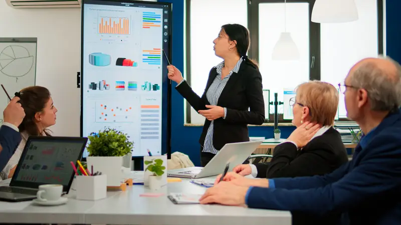 Presenter demonstrating AI dashboards on a large screen to a team in a meeting room, illustrating the gap between an impressive demo and everyday adoption